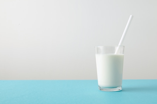 Transparentes Glas mit frischer Bio-Milch und weißem Trinkhalm innen lokalisiert auf pastellblauem Tisch