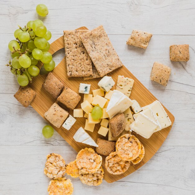 Trauben, Cracker, Knäckebrot und Käseblöcke über dem Holzschreibtisch