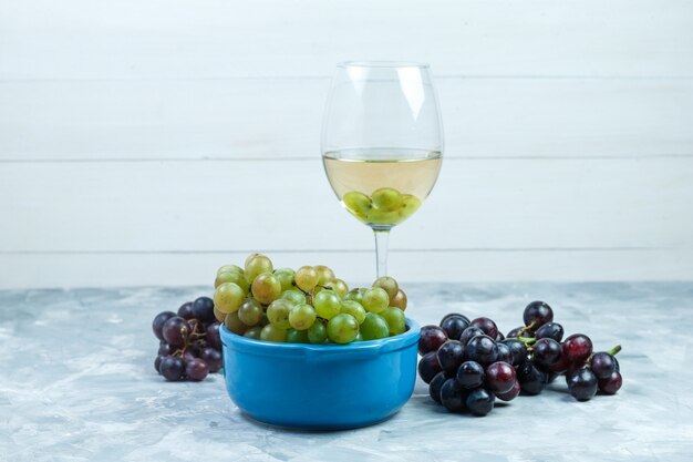 Trauben der Seitenansicht in der Schüssel mit einem Glas Wein auf grungy grauem und hölzernem Hintergrund. horizontal