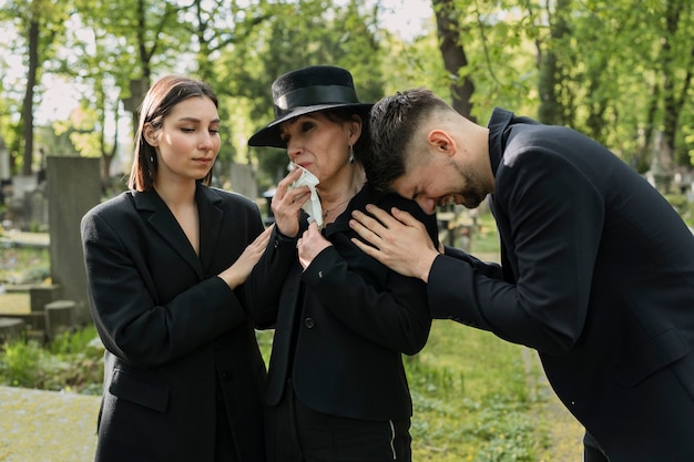 Trauernde Familie in Schwarz gekleidet, die an einem Grab auf dem Friedhof weint