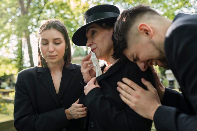 Trauernde Familie in Schwarz gekleidet, die an einem Grab auf dem Friedhof weint