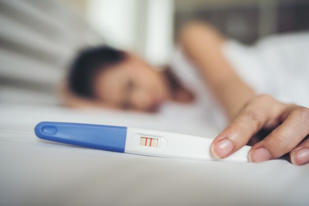 Traurige Frau, die beschwert, einen Schwangerschaftstest sitzend, der auf Bett sitzt