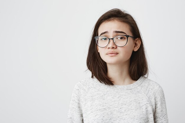 Traurige hübsche Frau, die sich verärgert fühlt, während sie Zeit allein zu Hause verbringt. Schöne junge dunkelhaarige Frau, die stilvolle Brillen trägt