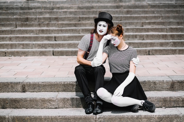 Traurige Pantomimepaare, die auf Treppenhaus sitzen