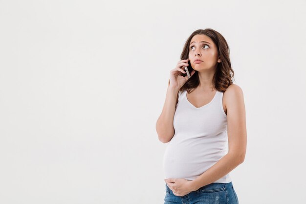 Traurige schwangere Frau isoliert, die durch Handy spricht