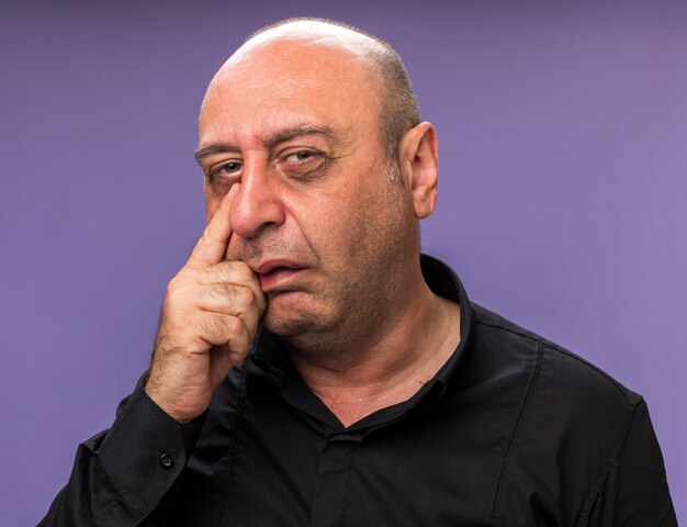 trauriger erwachsener kranker kaukasischer Mann legt Finger auf Augenlid isoliert auf lila Wand mit Kopienraum