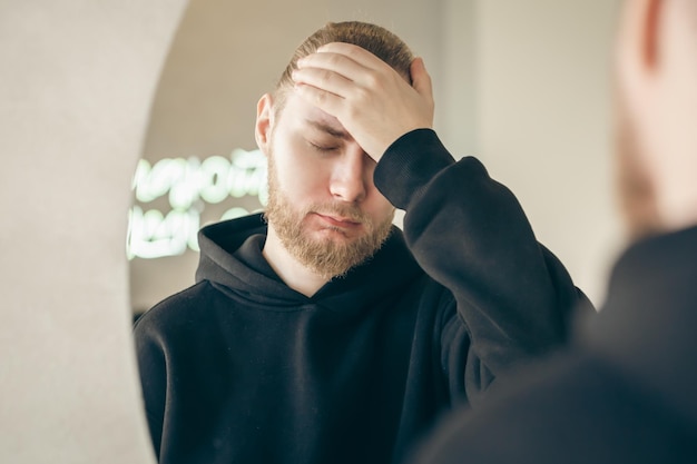 Kostenloses Foto trauriger junger mann mit bart vor einem spiegelkonzept für psychische gesundheit