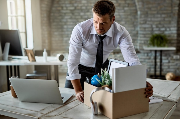 Trauriger Unternehmer, der seine Sachen in Kartons verpackt, während er das Büro verlässt, nachdem er seinen Job verloren hat