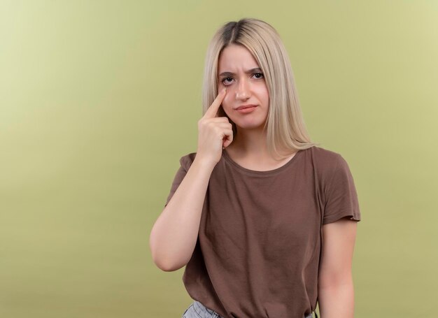 Trauriges junges blondes Mädchen, das Schrei mit Finger auf Auge auf isoliertem Grünraum mit Kopienraum gestikuliert