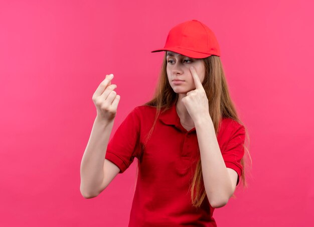 Trauriges junges Liefermädchen in der roten Uniform, die Geld tut und Geste auf isoliertem rosa Raum weint