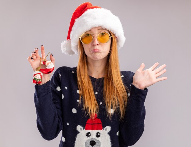 Trauriges junges schönes Mädchen, das Weihnachtshut trägt, der Weihnachtsspielzeug hält und Hände lokalisiert auf weißem Hintergrund verteilt