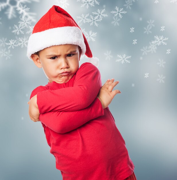 Trauriges Kind mit Weihnachtsmütze mit Schneeflocken Hintergrund