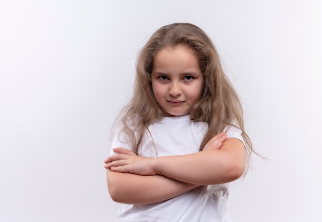 Trauriges kleines Schulmädchen, das weißes T-Shirt trägt, das Hände auf lokalisiertem weißem Hintergrund kreuzt