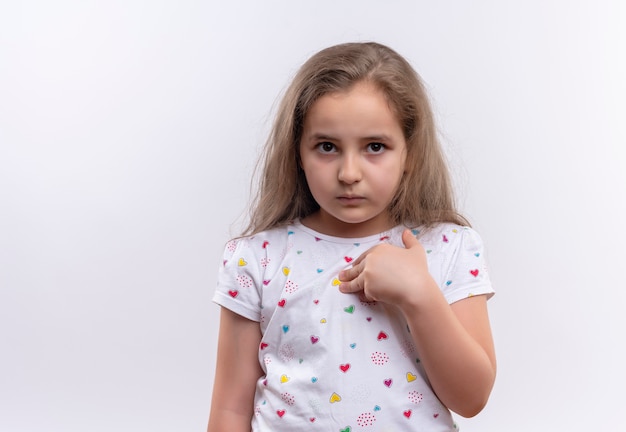 Trauriges kleines Schulmädchen, das weißes T-Shirt trägt, zeigt sich auf lokalisierten weißen Hintergrund