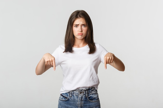 Trauriges und düsteres brünettes Mädchen schmollend und zeigte mit Bedauern mit den Fingern nach unten.