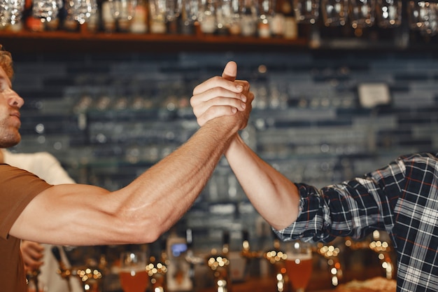 Treffen mit den besten Freunden. Zwei glückliche junge Männer in Freizeitkleidung sprechen und trinken Bier, während sie zusammen in der Bar sitzen.