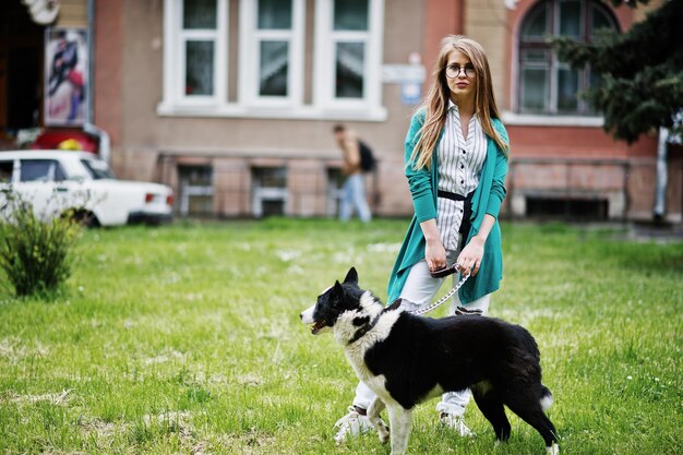 Trendiges Mädchen mit Brille und zerrissenen Jeans mit russoeuropäischem Laika Husky-Hund an der Leine gegen die Straße der Stadt Freund Mensch mit Tierthema