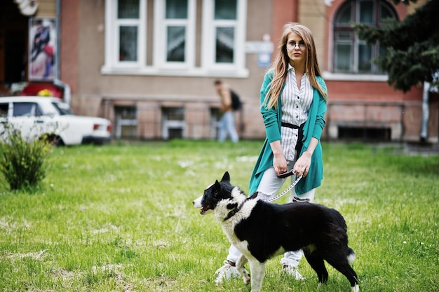 Trendiges Mädchen mit Brille und zerrissenen Jeans mit russoeuropäischem Laika Husky-Hund an der Leine gegen die Straße der Stadt Freund Mensch mit Tierthema