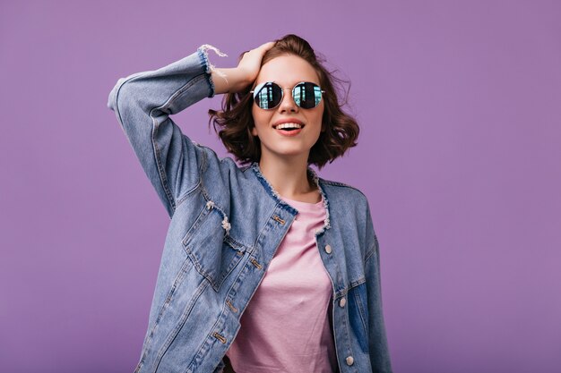 Trendy emotionale Frau in der glamourösen Kleidung lächelnd. Gut gekleidetes weißes Mädchen in der Sonnenbrille stehend.