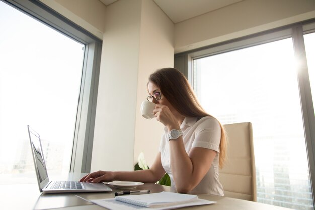 Trinkender Kaffee der schönen Geschäftsfrau beim Arbeiten an Laptop am Arbeitsplatz