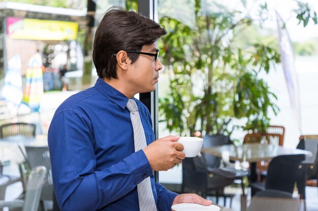 Trinkender Kaffee des asiatischen Geschäftsmannes, der an Plan denkt
