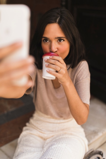 Trinkender Kaffee des Mädchens, der Selbstporträt vom intelligenten Telefon nimmt