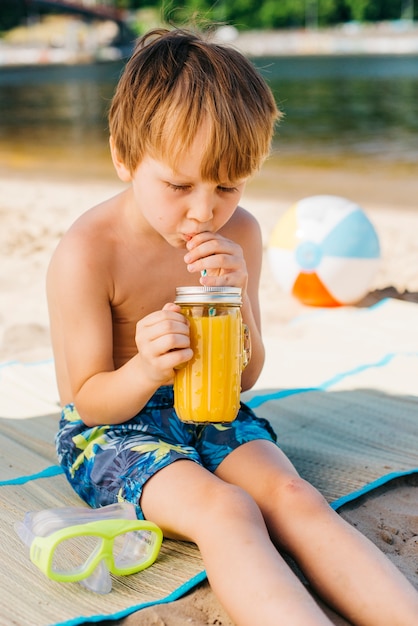 Trinkender Saft des kleinen Jungen auf Strand