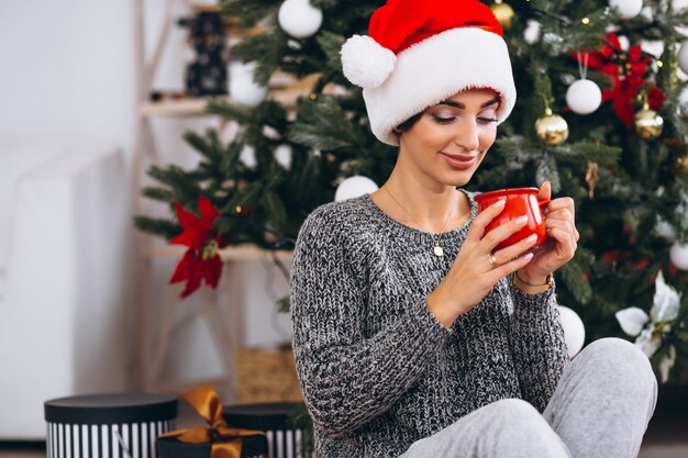 Trinkender Tee der Frau durch Weihnachtsbaum