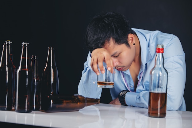 Trinkender Whisky des alkoholischen asiatischen Mannes mit vielen Flaschen