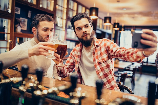 Trinkendes Bier des hübschen bärtigen Mannes zwei in der Kneipe