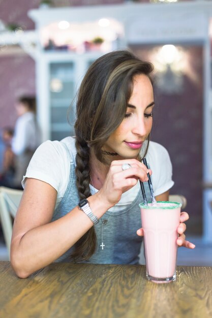 Trinkendes Milchshake der jungen Frau mit Stroh auf Tabelle