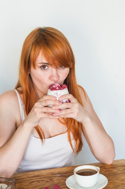 Trinkglas der jungen Frau der Rothaarigen Joghurt mit Himbeeren mit Kaffee auf Tabelle