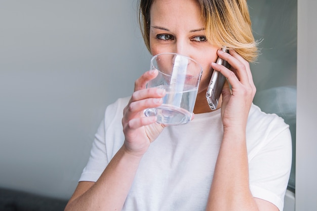 Trinkwasser der Frau und am Telefon sprechen