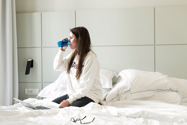 Trinkwasser der kühlen Frau auf Bett