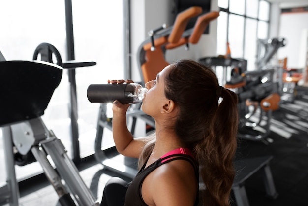 Trinkwasser der mittleren schussfrau im fitnessstudio