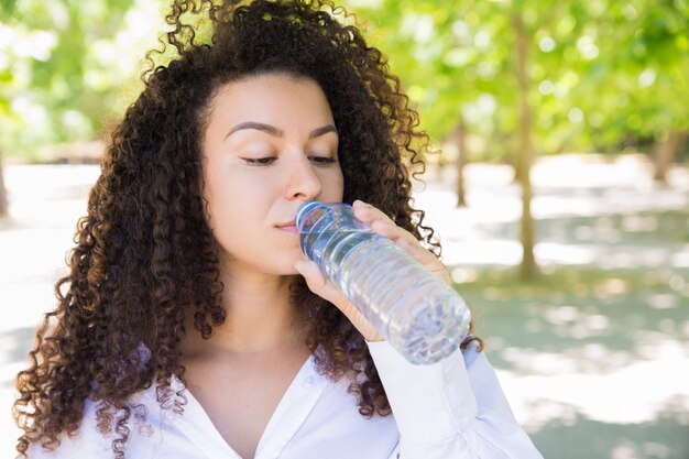 Trinkwasser der recht jungen Frau von der Flasche im Park