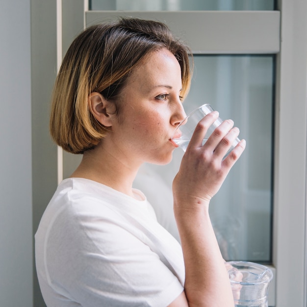 Trinkwasser der Seitenansichtfrau nahe Fenster