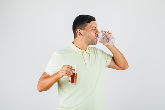 Trinkwasser des jungen Mannes beim Halten von Cola-Glas im T-Shirt