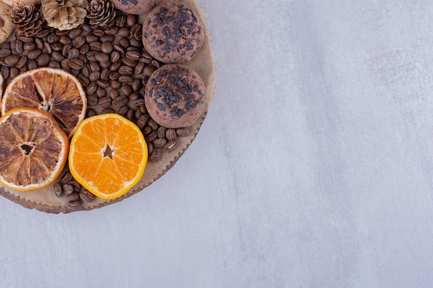 Trockene und saftige Orangenscheiben, Kaffeebohnen, Tannenzapfen und Kekse auf einem Brett auf weißem Hintergrund.