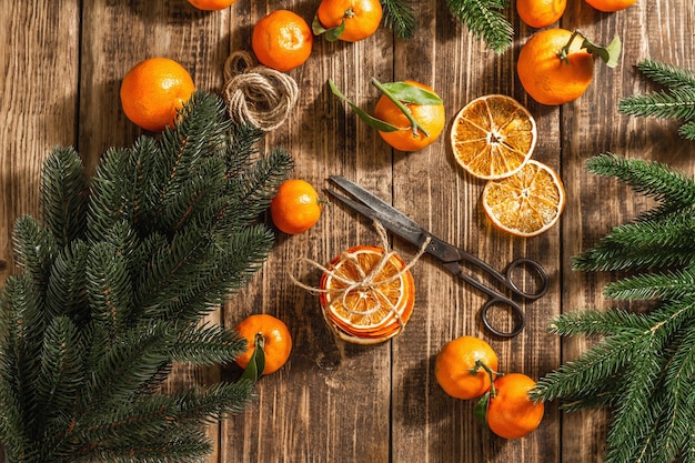 Trockener orangenscheiben-snack. getrocknete zitrusfrüchte für weihnachtsdekorationen. mandarinen mit blättern, tannenzweigen, schere und faden. hölzerner hintergrund, rustikales konzept, draufsicht Premium Fotos