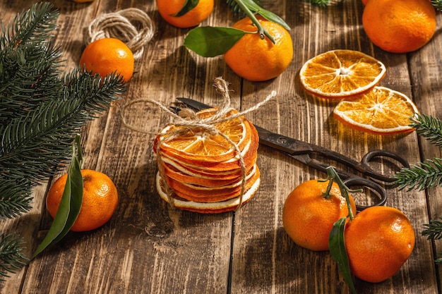 Trockener orangenscheiben-snack. getrocknete zitrusfrüchte für weihnachtsdekorationen. mandarinen mit blättern, tannenzweigen, schere und faden. hölzerner hintergrund, rustikales konzept, kopienraum Premium Fotos