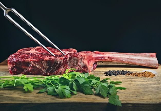 Trockenes gealtertes Wagyu-Tomahawk-Steak auf einem Holzschneidebrett mit Gewürzen und Petersilie