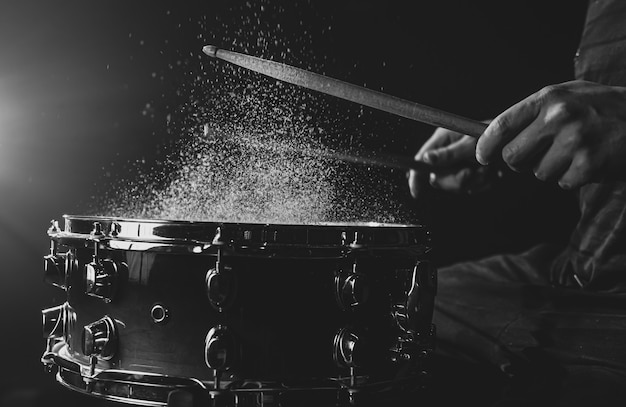 Trommelstöcke schlagen Snare-Drum mit Spritzwasser auf schwarzem Hintergrund unter Bühnenbeleuchtung.