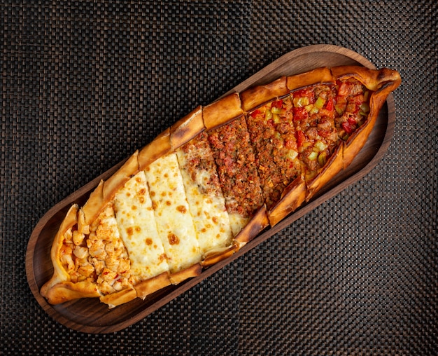 Türkische pide mit gefülltem fleisch, käse und hühnchenstücken auf einer holzschale