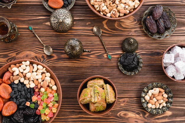 Türkisches Ramadan-Dessert-Baklava; Lukum; Termine; Trockenfrüchte und Nüsse auf irdenen und metallischen Schüsseln am Schreibtisch aus Holz
