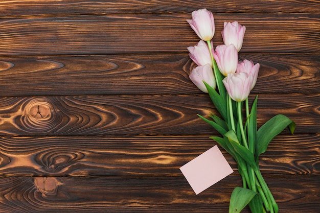 Tulpen und Karte mit leerem Aufkleber auf dunkler Tabelle