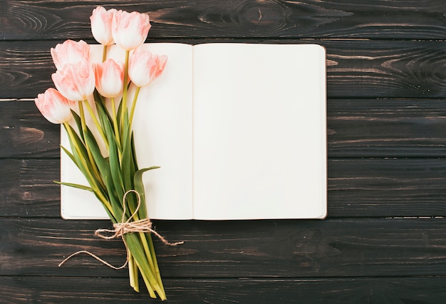Tulpenblumenstrauß mit leerem Notizbuch auf Tabelle