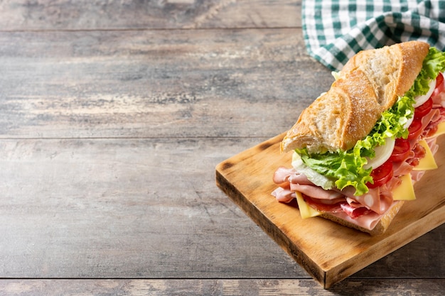 U-Boot-Sandwich mit Schinken, Käse, Salat, Tomaten, Zwiebeln, Mortadella und Wurst auf Holztisch