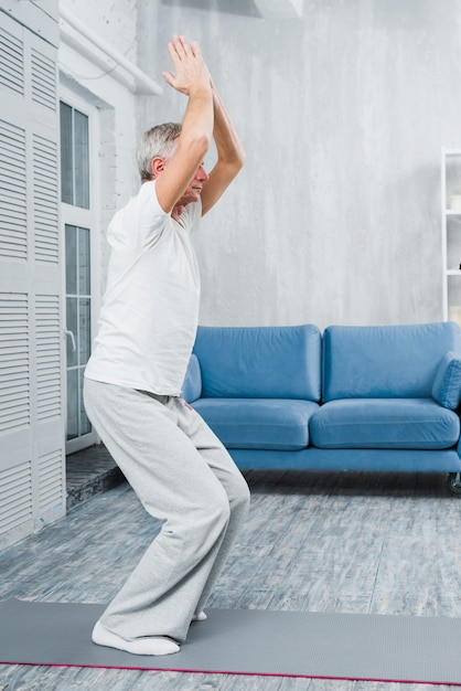 Übendes Yoga des sportlichen älteren Mannes zuhause