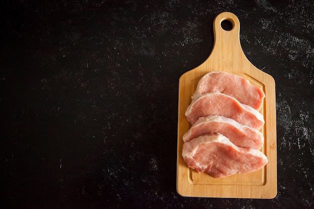 Kostenloses Foto Über der draufsicht von vier frischen rohen steaks auf holzbrett auf schwarzem holzhintergrund. gourmet-essen und frische rohkost